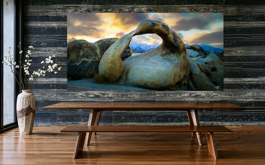 Large TV screen displaying a scenic landscape with rocks, placed above a wooden table in a room with wooden flooring.