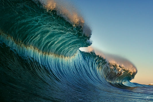 Close-up of a powerful teal ocean wave forming a hollow barrel with golden sunrise spray against a clear sky; dramatic surf seascape wall art