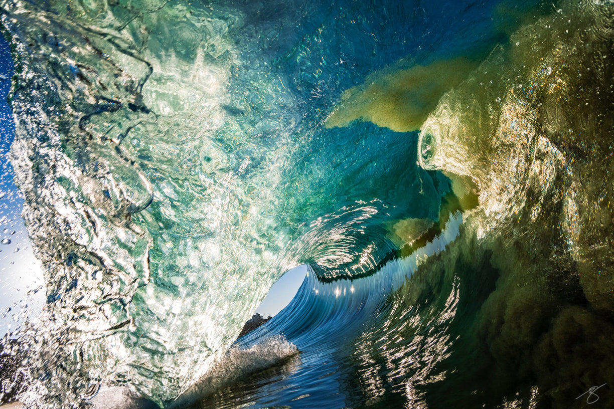 Underwater surf photo from inside a curling emerald wave at sunrise, with sparkling highlights and sand swirling beneath