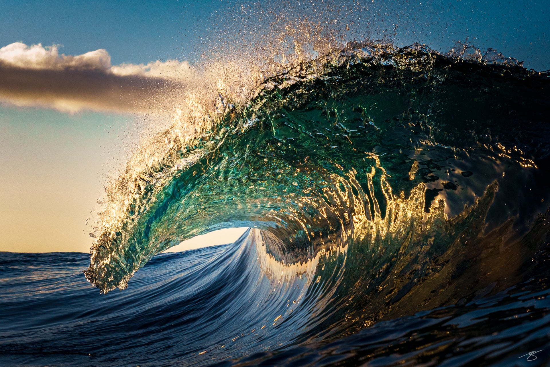 Sunrise photo of a teal barrel wave with golden light glowing inside the curl against a clear sky