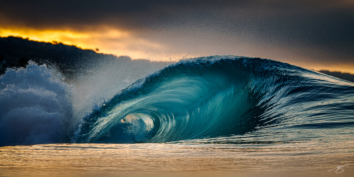 Glassy emerald barrel wave curling at sunrise with golden reflections and spray under dark clouds along the coast