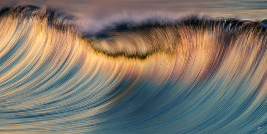 Abstract long-exposure photo of a wave at sunset, golden highlights sweeping into indigo curves in a panoramic seascape