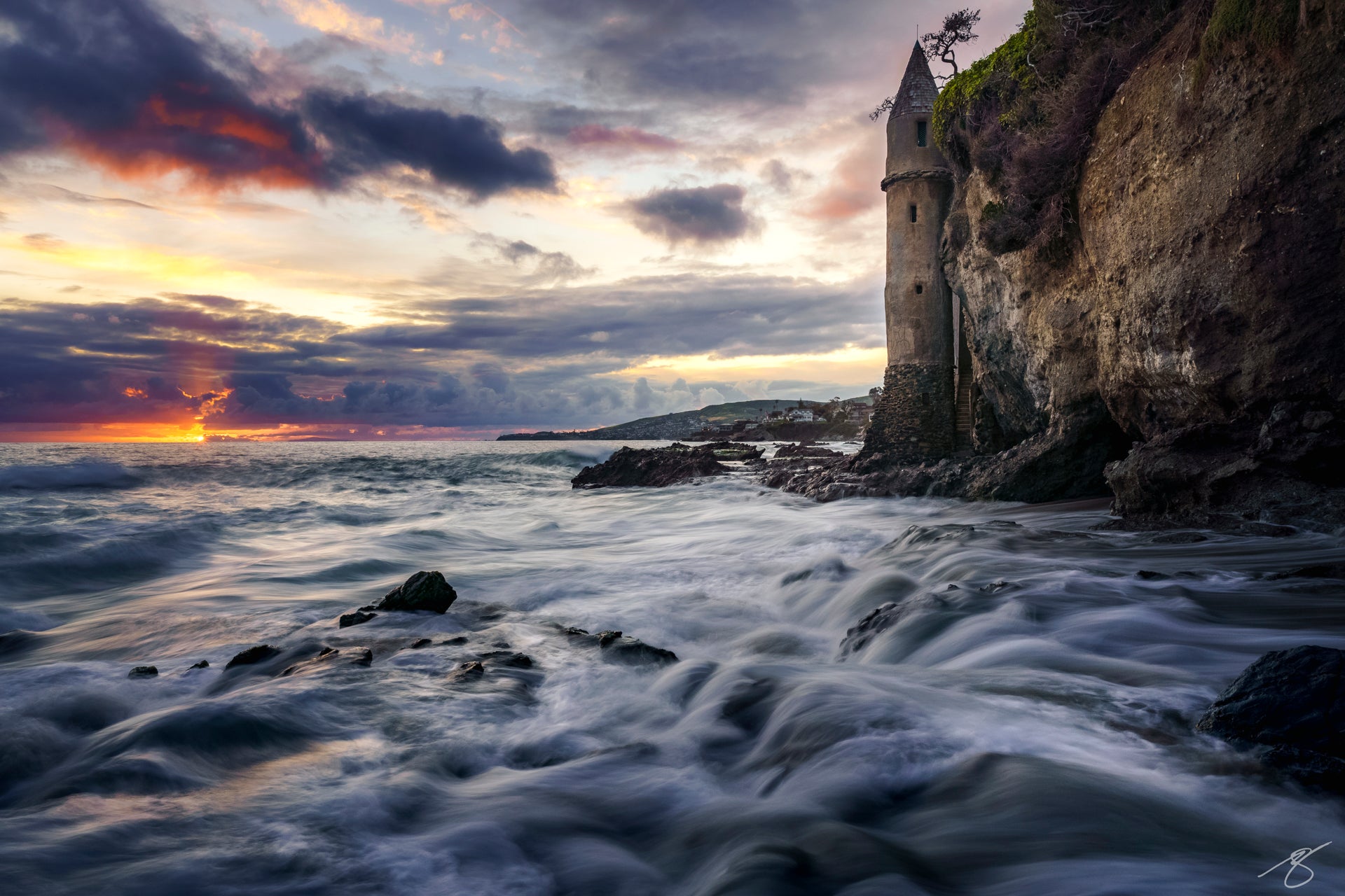 Stormy sunset at Laguna Beach’s Victoria Beach with waves swirling around the stone Pirate Tower on the cliff