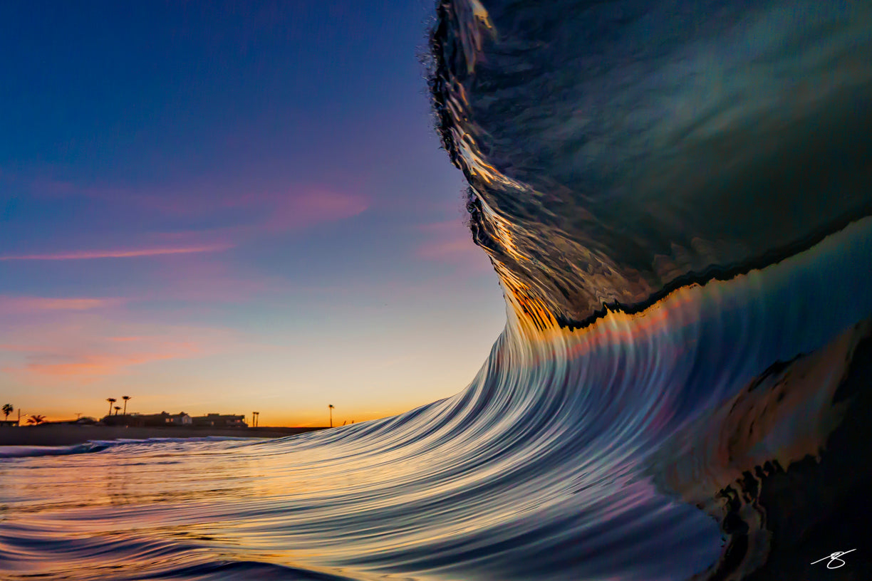 Waterline photo of a glassy wave curling at sunset, with silky reflections and distant palms along the shore; fine art ocean photograph