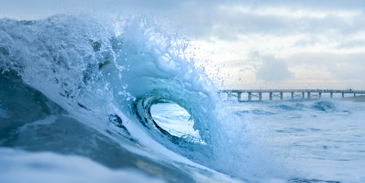 Breaking wave near a pier at sunrise, fine art ocean photography print by Beau Jesse Johnston.