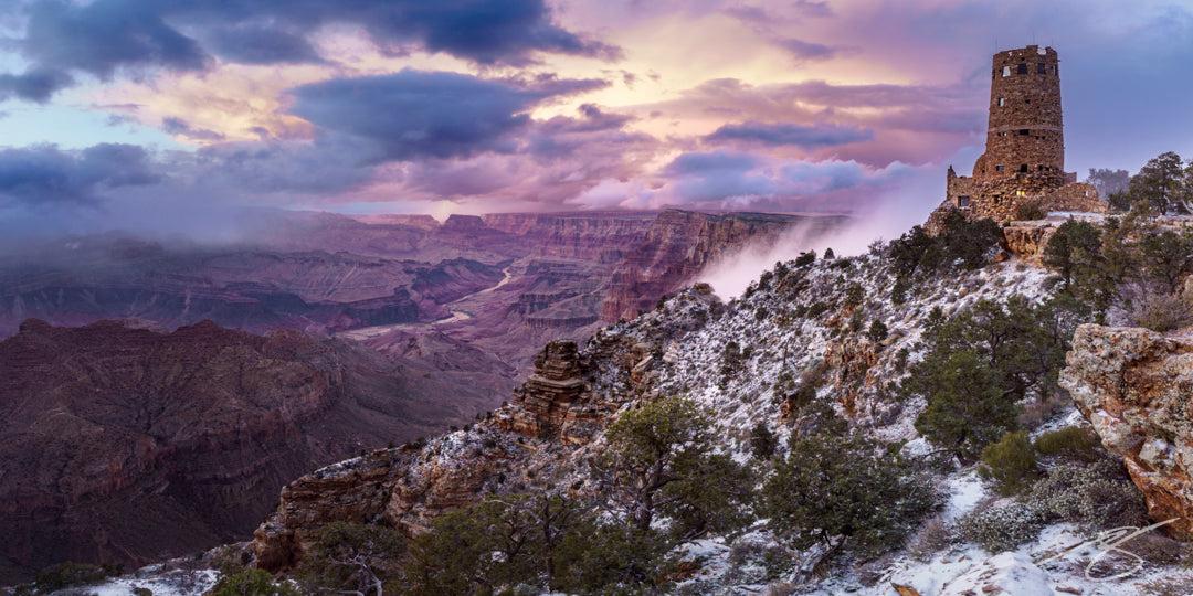 Panoramic winter view of the Grand Canyon at sunset with the Desert View Watchtower, snow on the rim, clouds, and the Colorado River winding below