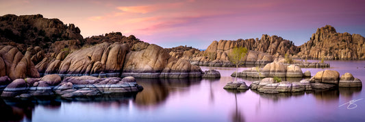 Panoramic long-exposure of Watson Lake’s Granite Dells at sunset, pastel pink-lavender sky reflecting on still water with rounded boulders and small trees