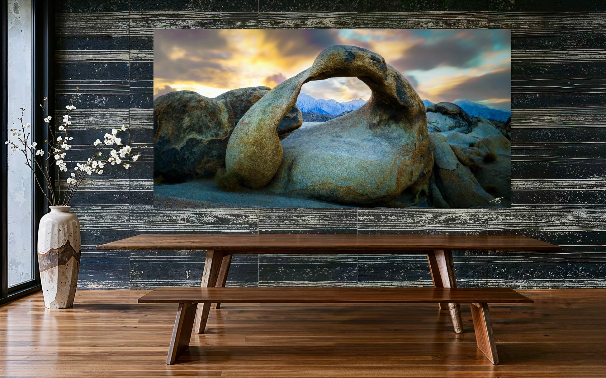 Large TV screen displaying a scenic landscape with rocks, placed above a wooden table in a room with wooden flooring.