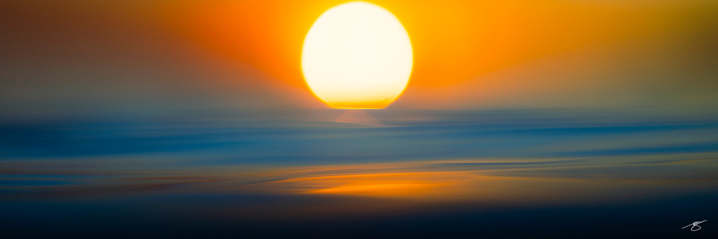 Minimalist fine art seascape featuring a glowing golden sun above softly blurred ocean waves. Blue and orange hues blend together using intentional camera motion to create a serene, abstract sunset scene emphasizing color, light, and tranquility.