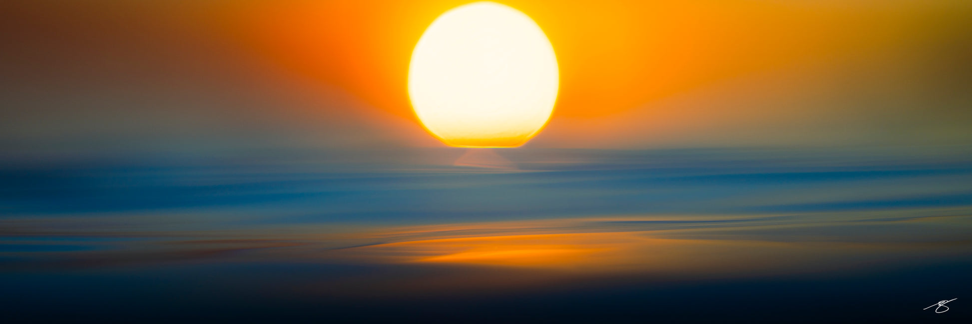 Minimalist fine art seascape featuring a glowing golden sun above softly blurred ocean waves. Blue and orange hues blend together using intentional camera motion to create a serene, abstract sunset scene emphasizing color, light, and tranquility.