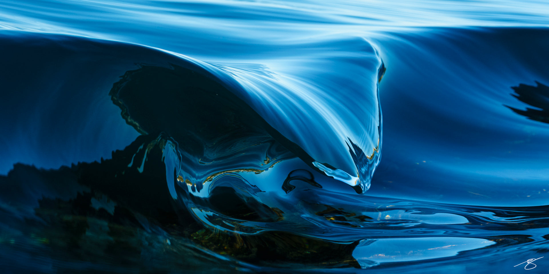 A close-up abstract photograph of a cresting ocean wave, rendered in rich cobalt and deep blue tones. Smooth, glass-like textures shape the wave into a sculptural form, highlighting fluid motion, reflections, and the elegant curves of water frozen in a fleeting moment.