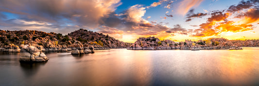 Panoramic sunset photograph of Watson Lake in Prescott, Arizona, showing smooth reflective water and the Granite Dells’ rounded pink boulders under glowing clouds
