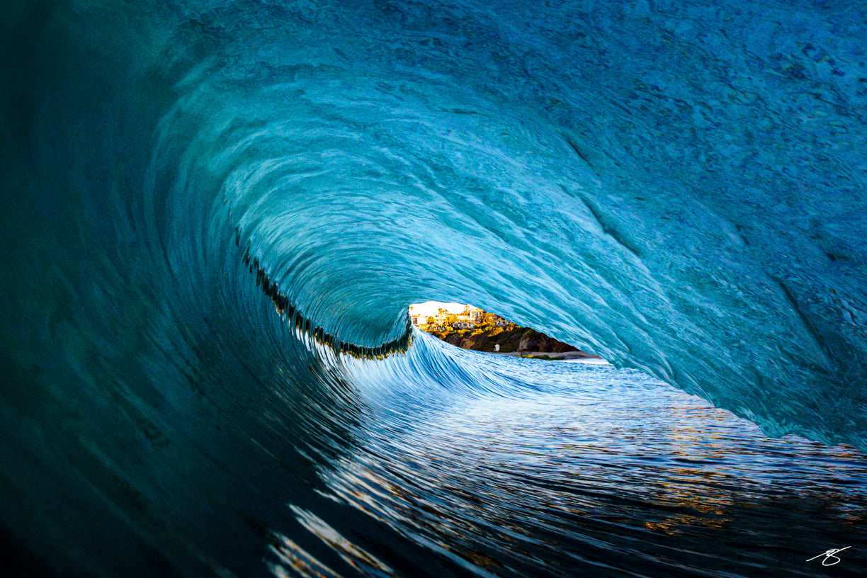 Fine art ocean wave barrel photography with coastal view framed inside the wave tunnel at sunset