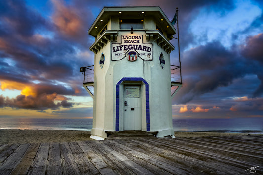 Historic Laguna Beach lifeguard tower on Main Beach at sunrise with dramatic clouds and wood boardwalk in the foreground