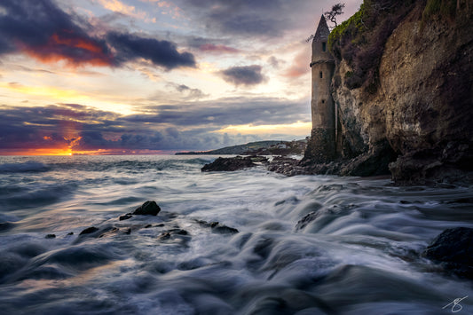Stormy sunset at Laguna Beach’s Victoria Beach with waves swirling around the stone Pirate Tower on the cliff