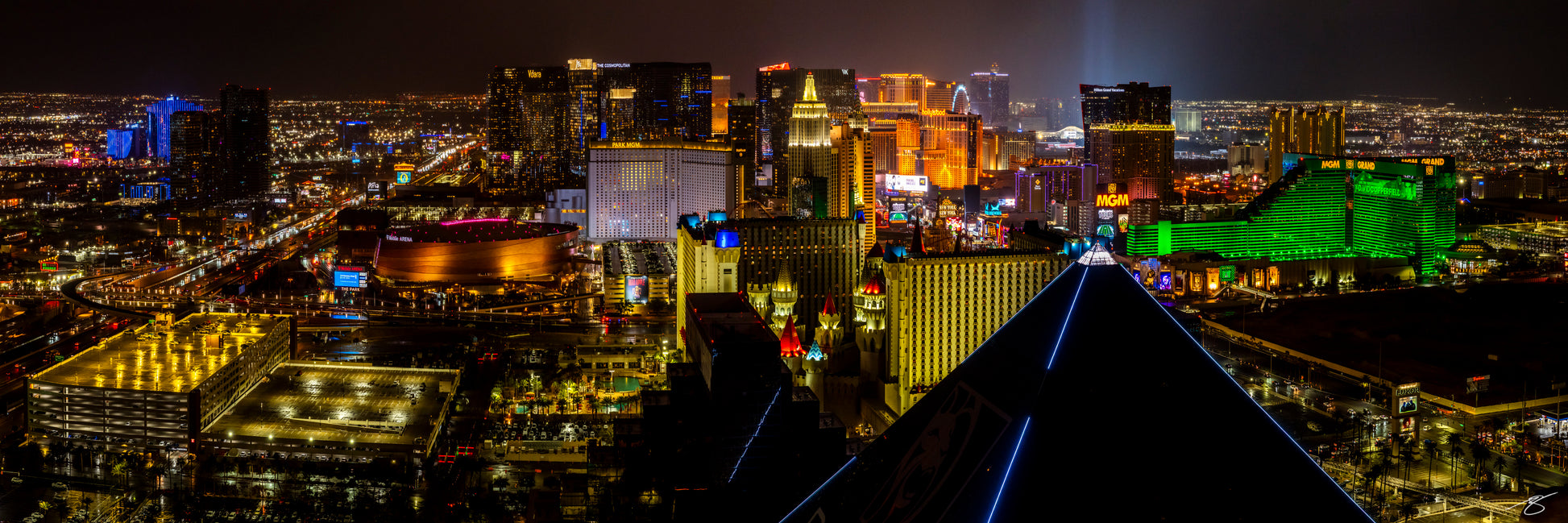 Fine art night panorama of the Las Vegas Strip captured from the Luxor Pyramid, showcasing glowing casinos, neon signs, wet streets, and expansive city lights stretching into the desert. A vibrant and dramatic urban cityscape under the night sky.