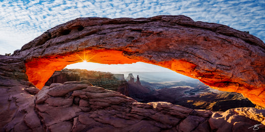 Sunrise through Mesa Arch in Canyonlands National Park, glowing orange beneath the arch with rugged canyons and spires in the distance