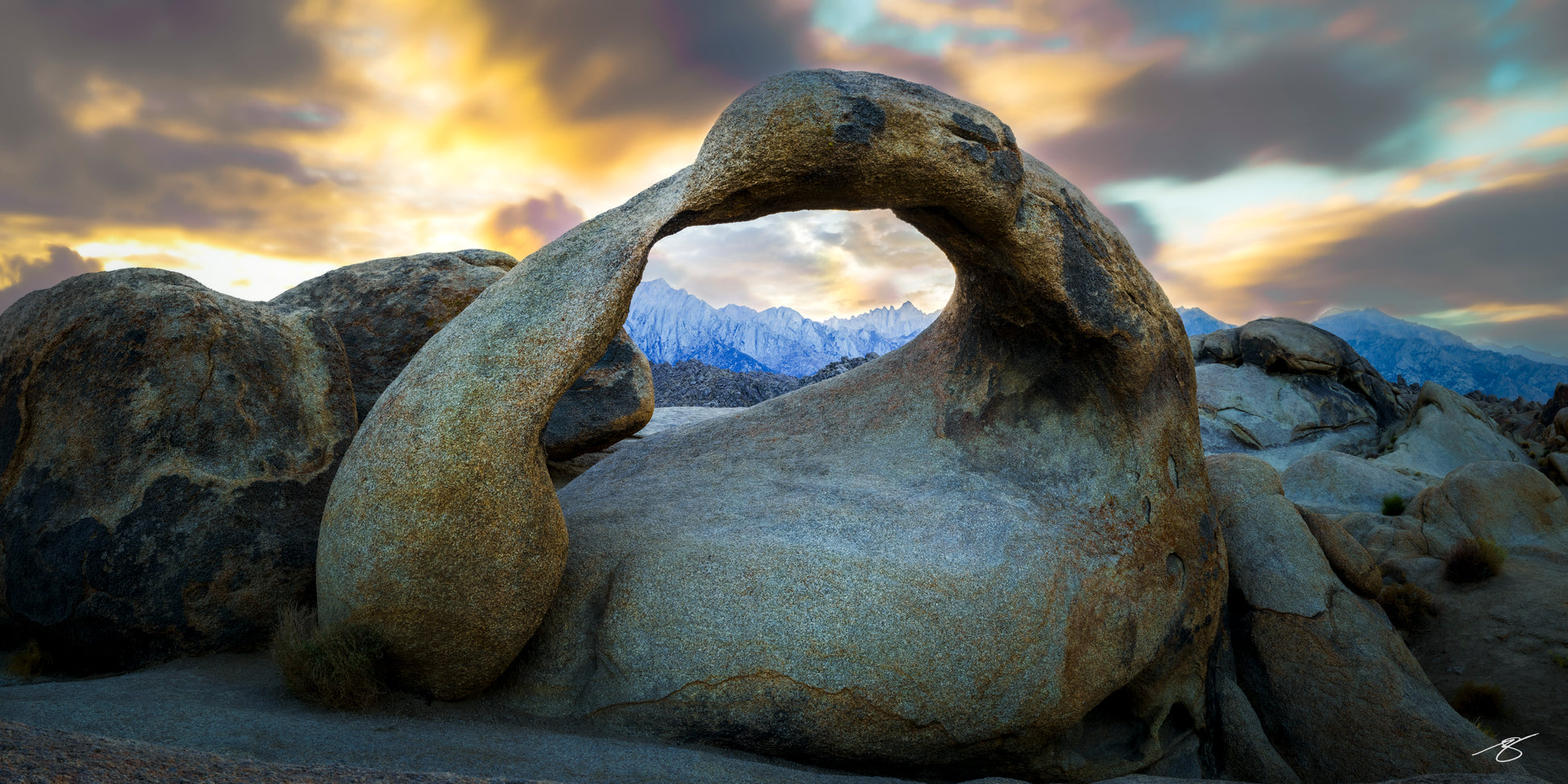 Fine art sunrise photograph of Mobius Arch in Alabama Hills, capturing its curved granite frame around the distant Sierra Nevada peaks. Soft warm light and long-exposure clouds create a dramatic and elegant landscape scene with rich textures and natural colors.