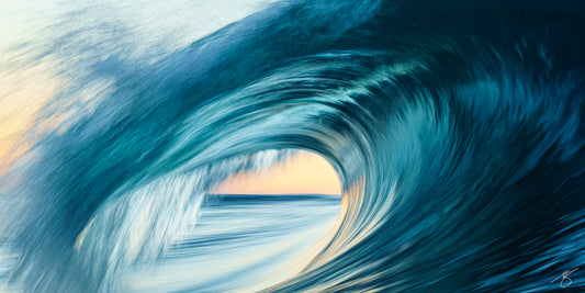 Abstract long-exposure of a curling ocean barrel at sunrise with teal blues and a warm golden glow visible through the wave