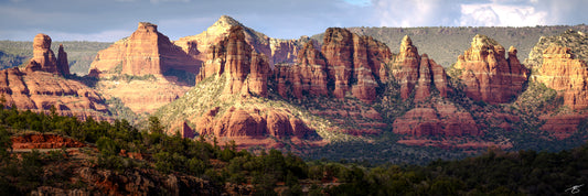 Wide panorama of Sedona’s iconic red rock cliffs and buttes illuminated by golden afternoon sunlight. Layers of sculpted sandstone rise above a forested desert foreground, creating a dramatic and detailed Southwest fine art landscape.
