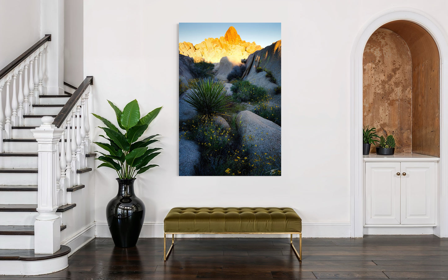 Staircase with a green bench, black vase, and a large mountain landscape painting on a white wall.