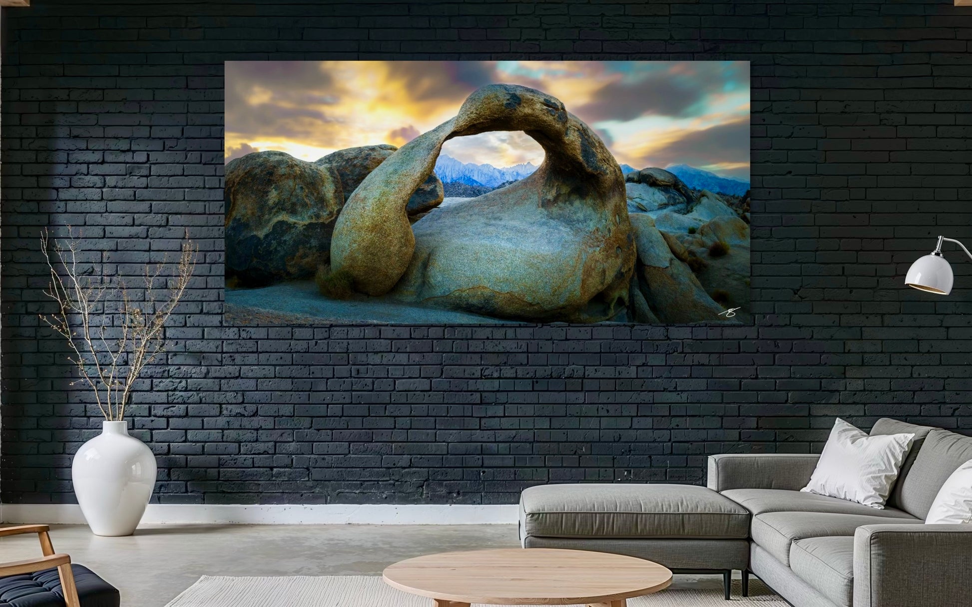 Living room with a large TV displaying a scenic rock formation, black brick wall, white vase, and gray sofa.