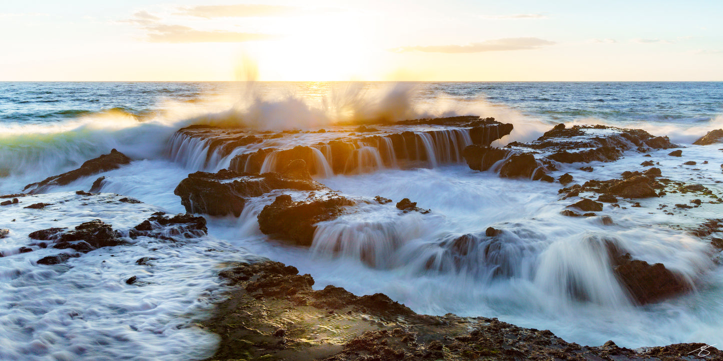 Long-exposure seascape of waves cascading over coastal rock formations at sunset in Laguna Beach. Golden light backlights the ocean spray as tidal waterfalls flow across the rugged shoreline, creating a dramatic fine art coastal scene.