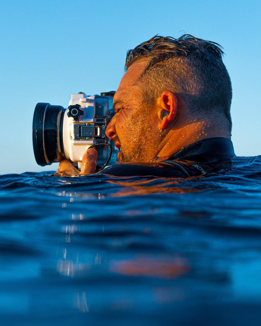 Fine art photographer Beau Johnston photographing ocean waves from the water with a professional camera in a waterproof housing during golden hour.