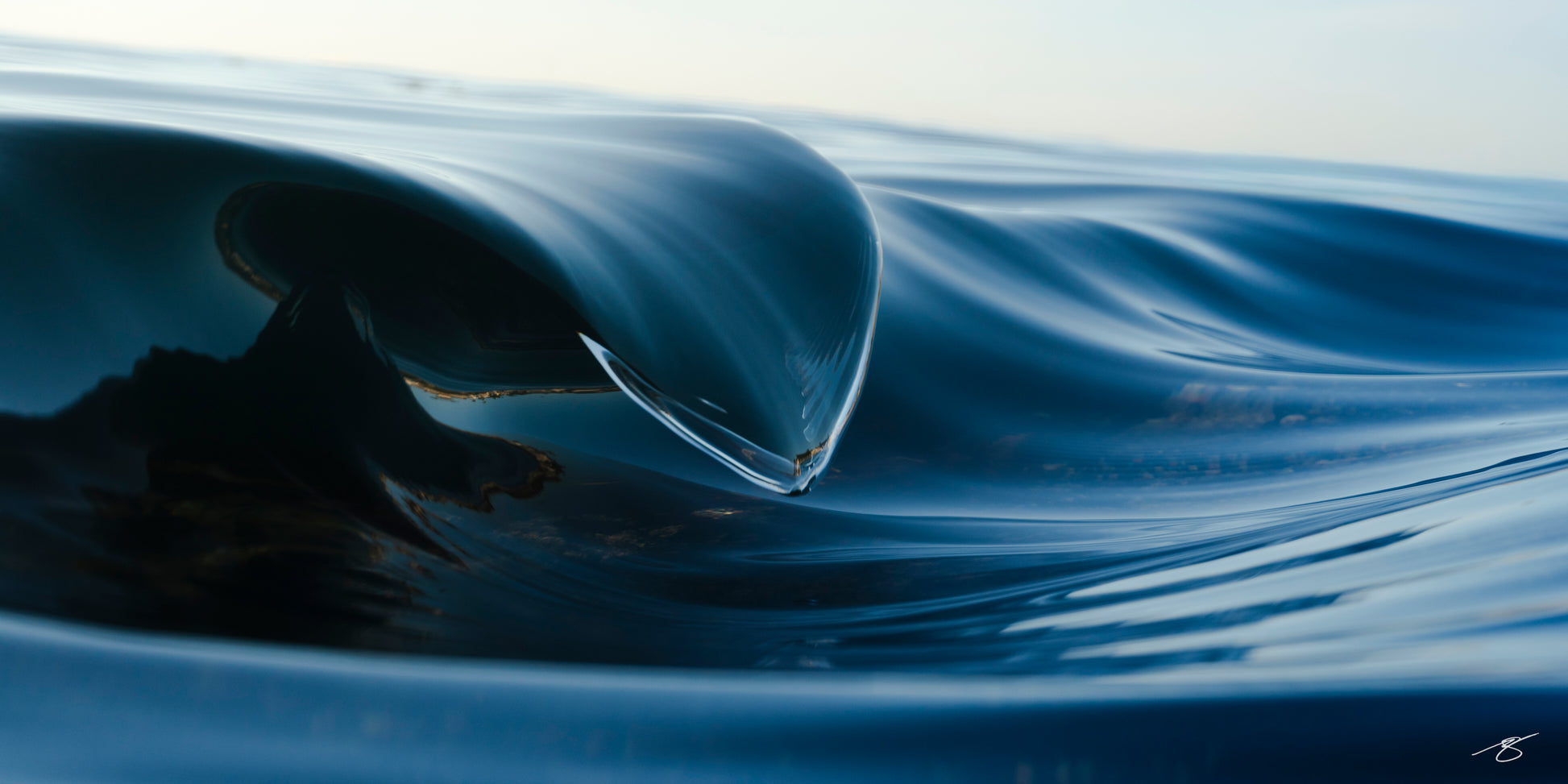 Blue abstract ocean wave photographed from within the Pacific Ocean, featuring a smooth glasslike curl and deep blue reflections by fine art photographer Beau Jesse Johnston.