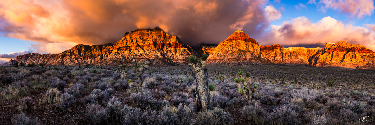 Panoramic view of Desert Cathedral featuring glowing red sandstone peaks beneath dramatic storm clouds at sunrise in Red Rock Canyon, Nevada.