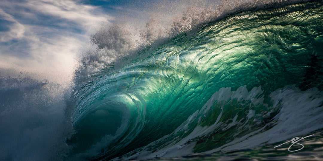 Close-up of a backlit emerald barrel wave with textured glassy surface and spraying lip beneath a moody sky; dramatic ocean fine art photograph