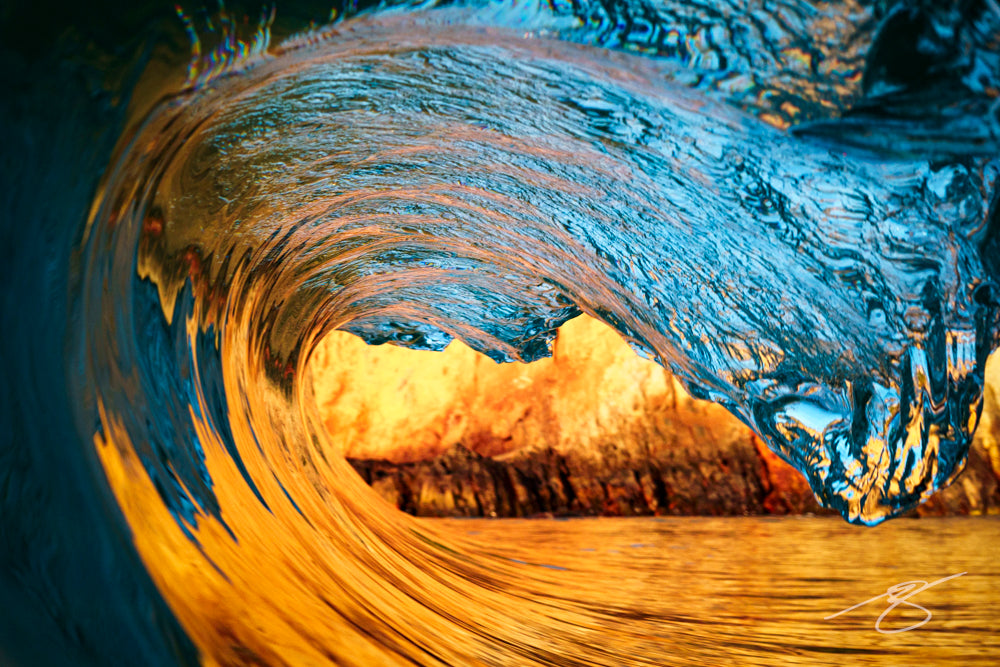 Close-up of a translucent wave forming a barrel with golden cliff reflections on the water at sunset; coastal fine art photograph