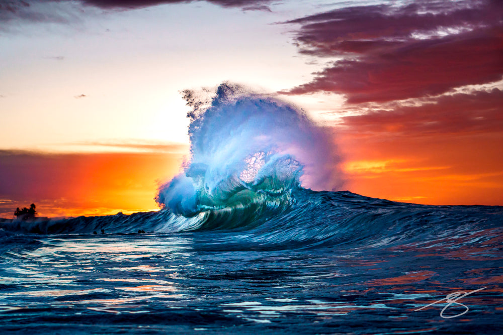 Backlit wave exploding at sunset, plume of spray rising against a fiery sky with rippled sea reflections; dramatic coastal fine art photograph